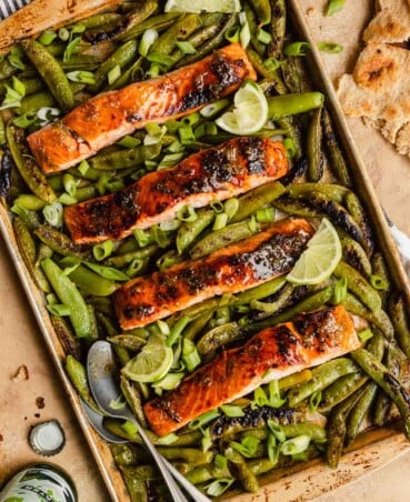 glazed salmon fillets on a baking sheet surrounded by snap peas.