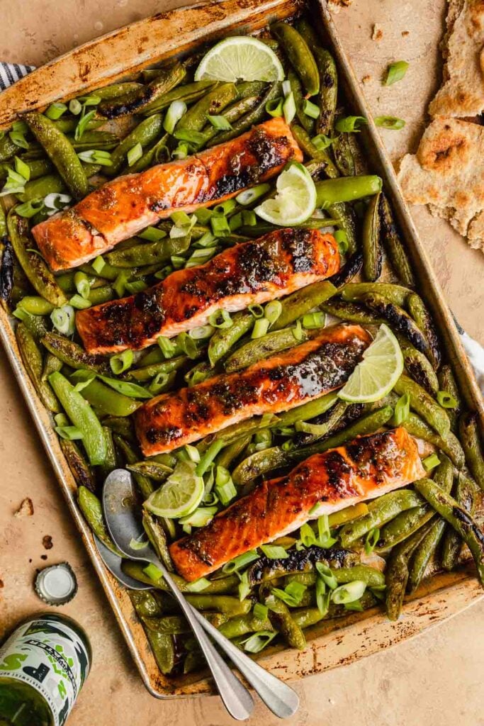 glazed salmon fillets on a baking sheet surrounded by snap peas.