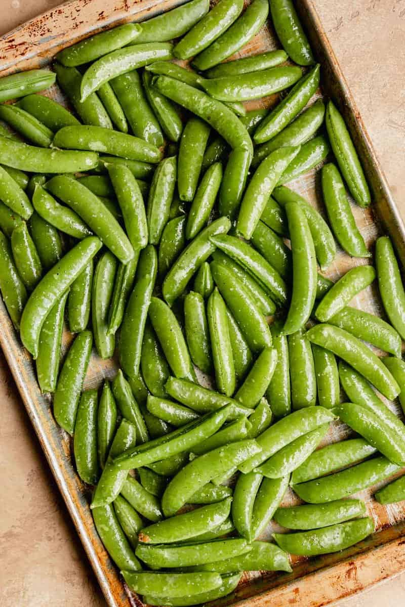 fresh snap peas coated in oil on a sheet pan