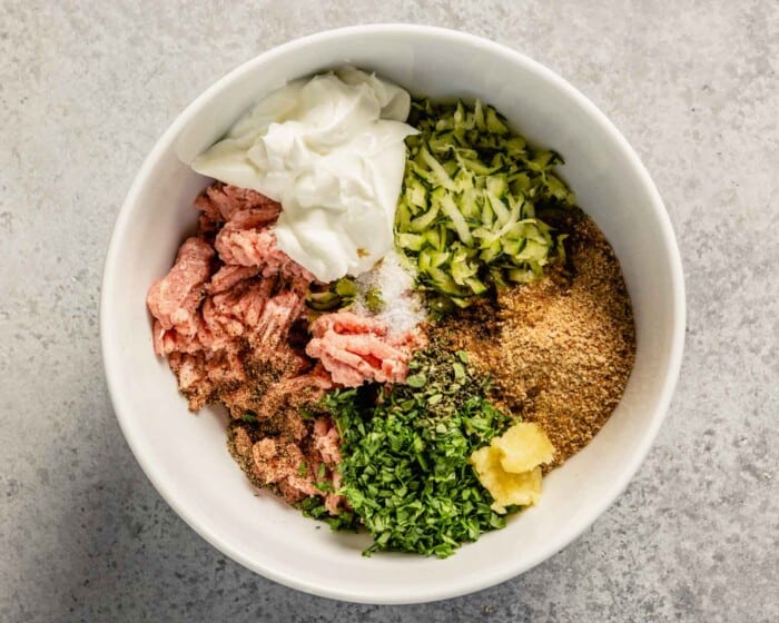 breadcrumbs, shredded zucchini, herbs, yogurt and ground turkey in a white mixing bowl