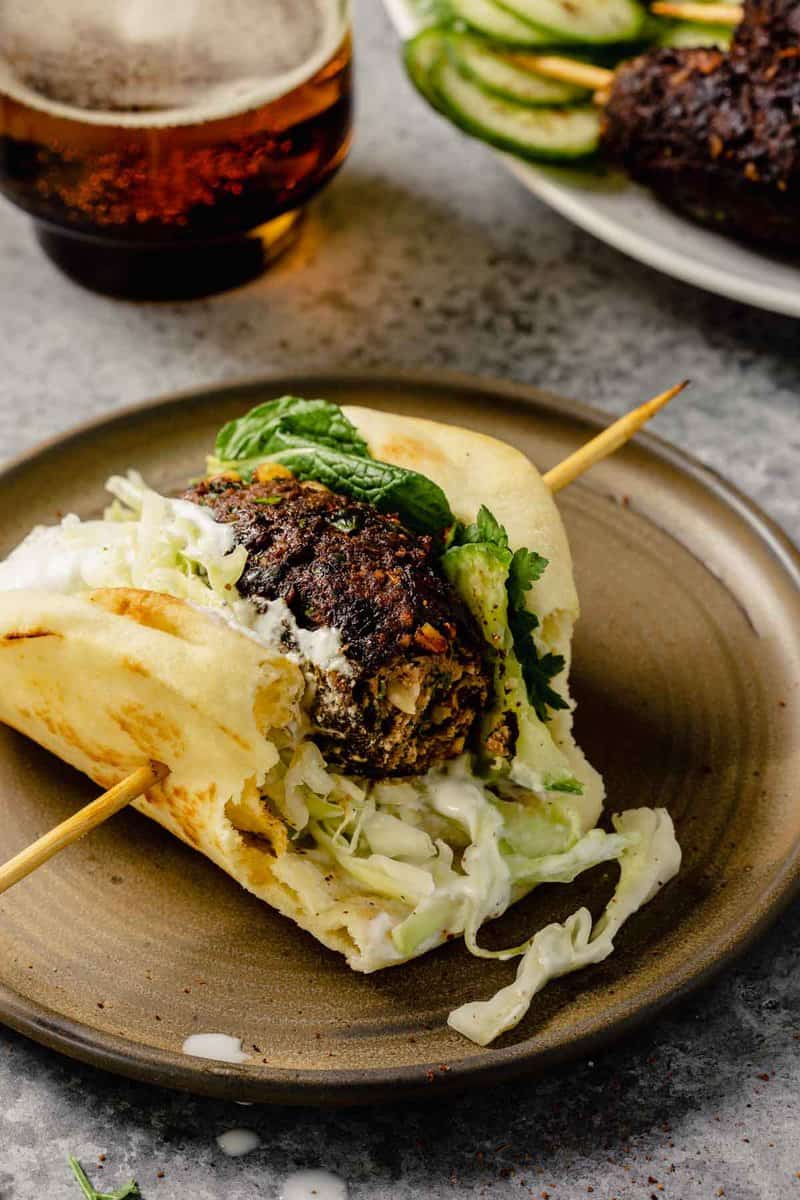 lamb kofta on a piece of naan bread topped with shredded cabbage, yogurt sauce, herbs and cucumber