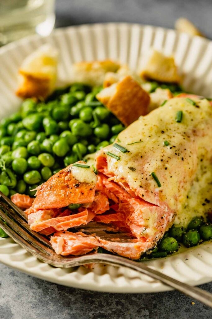 white scalloped plates filled with green peas, salmon topped with butter, croutons and herbs.