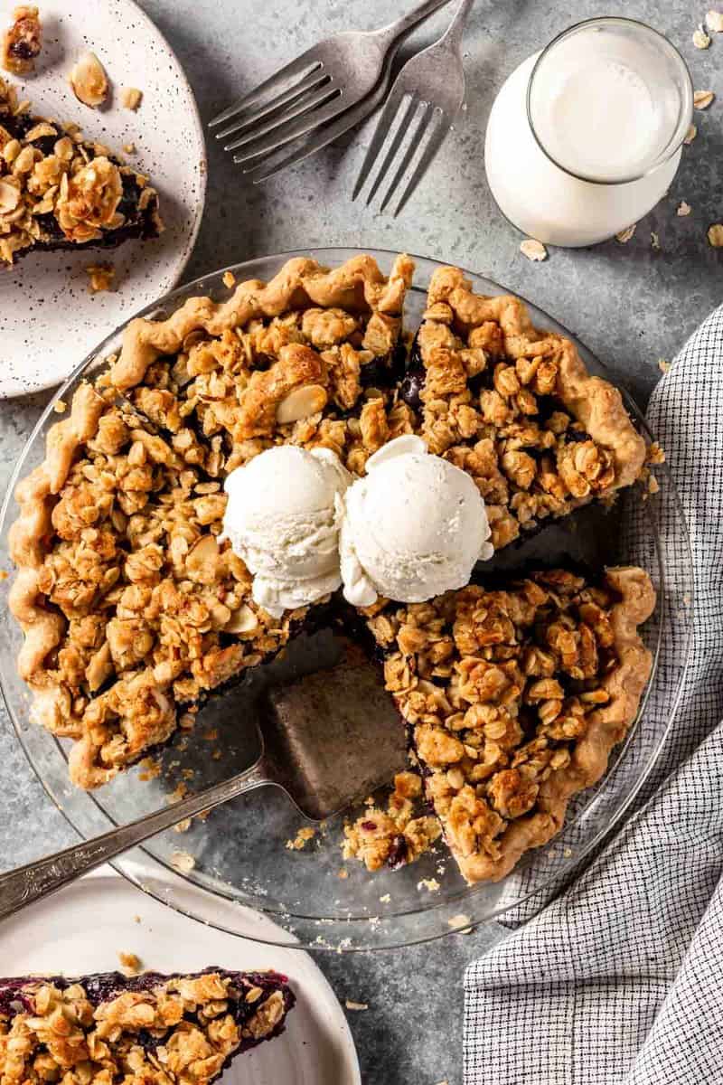 a blueberry crumble pie with slices taken out and scoops of ice cream on top of the pie
