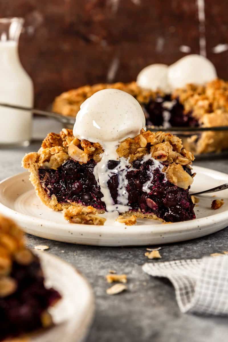 pie of blueberry pie on a white plate with a scoop of melty vanilla ice cream on top