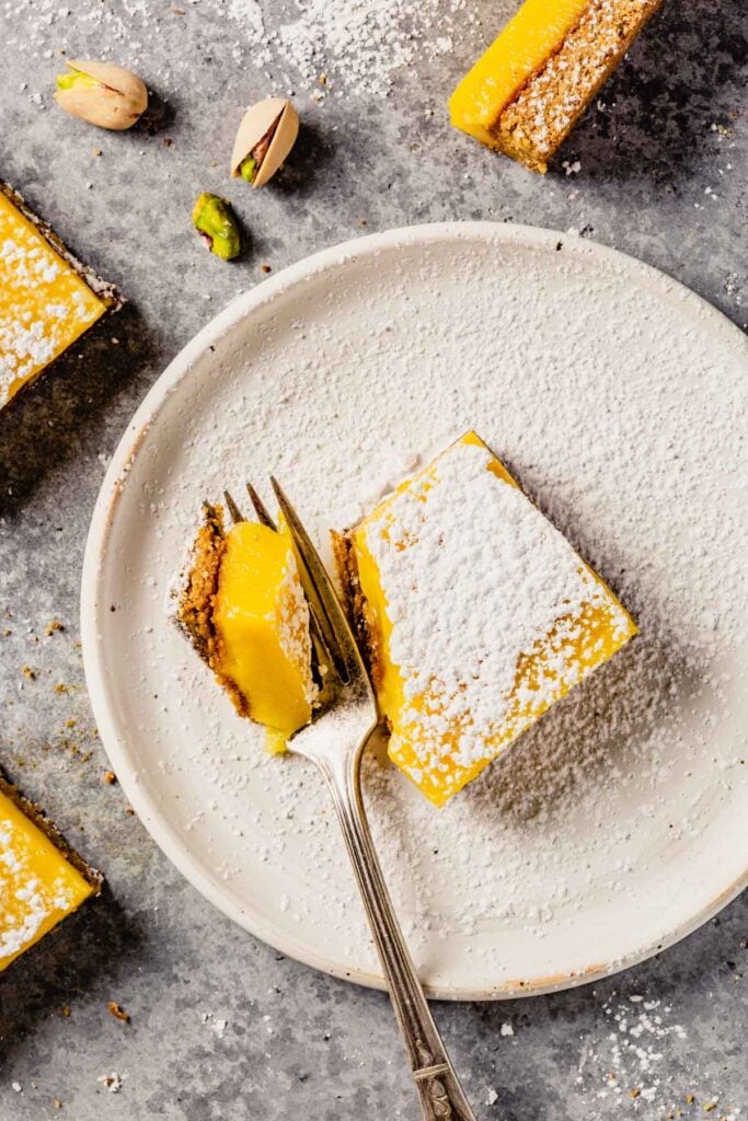 a lemon bar dusted with confectioners' sugar set in a white plate with a fork