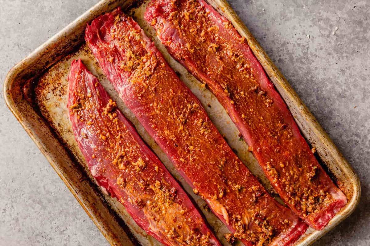 flank steak strips covered in a rub on a baking sheet