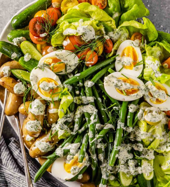 large white platter filled with butter lettuce, blanched green beans, fingerling potatoes, halved cherry tomatoes, mini cucumbers, hard boiled eggs and a creamy ranch dressing