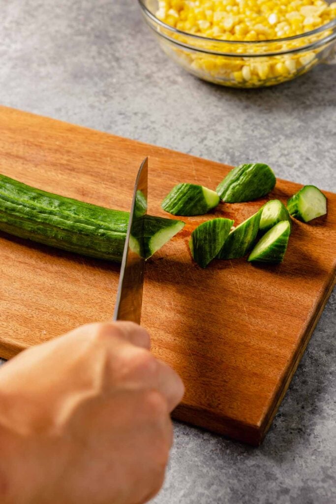 cucumber being cut on a brown wood cutting board