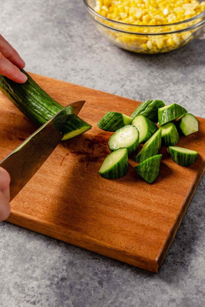 cucumber being cut on a brown wood cutting board