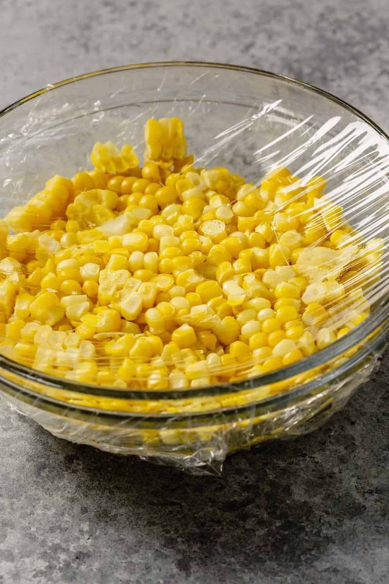 sweet corn in a glass bowl with plastic wrap on top