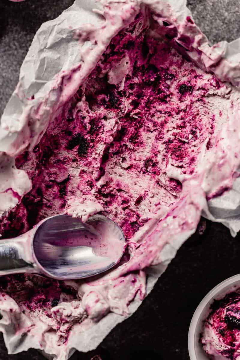 Swirled cherry ice cream in a loaf pan with scoops taken out and placed in small white bowls.