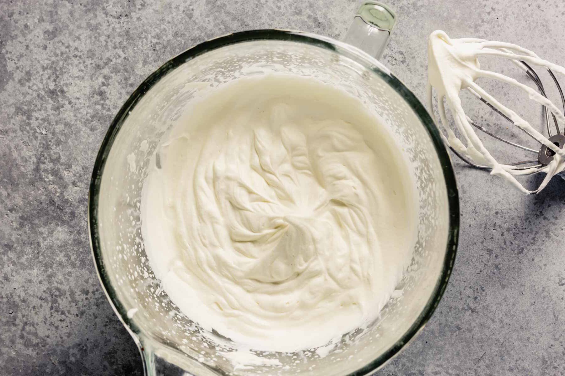 Whipped cream in a glass mixing bowl with the whisk attachment set off to the side. 