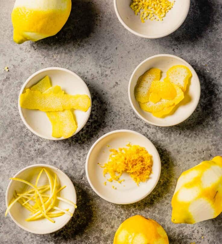 zested lemons set around small white bowls filled with minced lemon zest, peeled lemon zest and strips of lemon zest