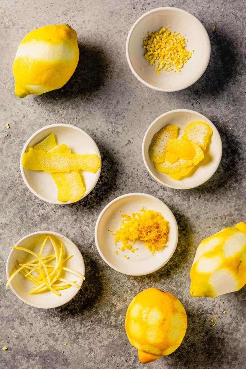 zested lemons set around small white bowls filled with minced lemon zest, peeled lemon zest and strips of lemon zest