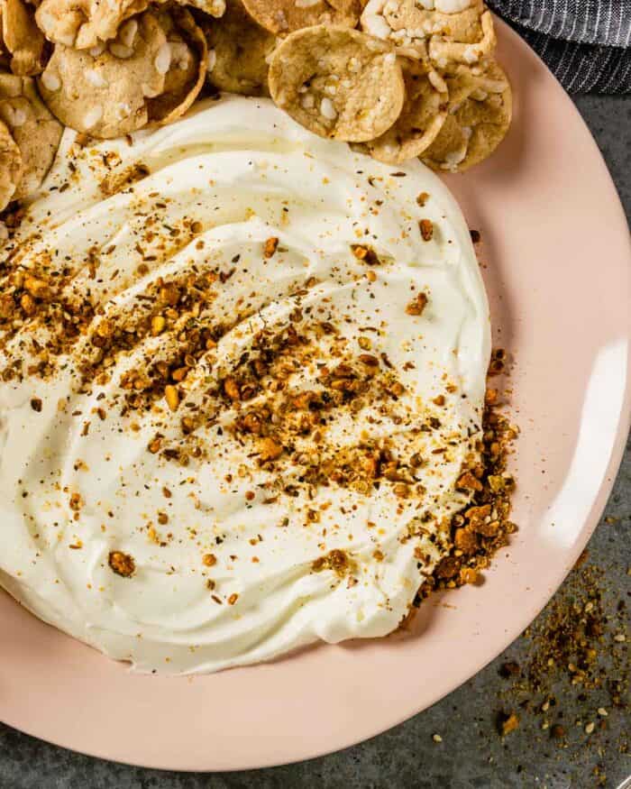 pink round plate with creamy white dip topped with a nut and spice seasoning 