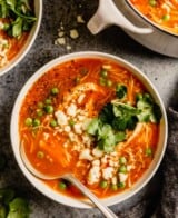 tomato soup with shredded chicken, peas, cilantro and crumbled cheese set on a table with a white pot filled with soup
