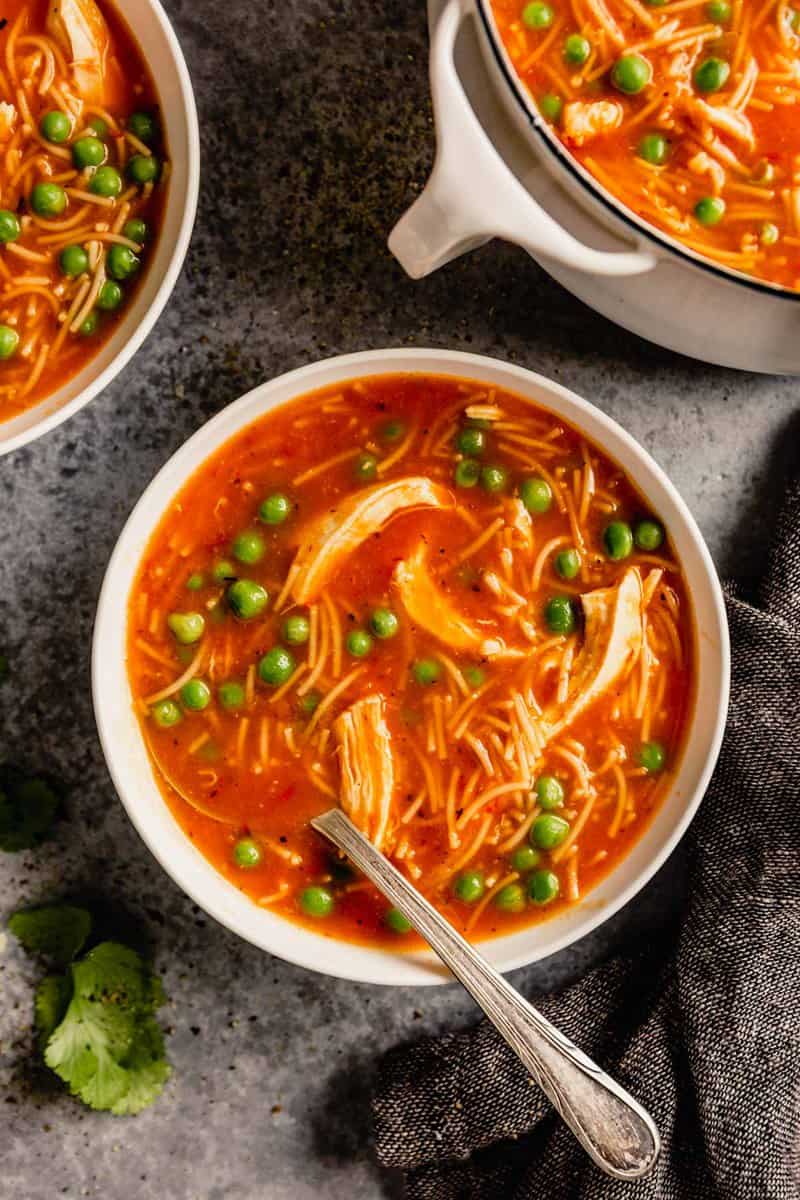 tomato soup with shredded chicken, peas and cilantro set on a table with a white pot filled with soup