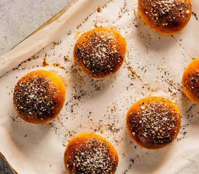 golden brown dinner rolls with seasoning on top set on a baking sheet lined with parchment paper