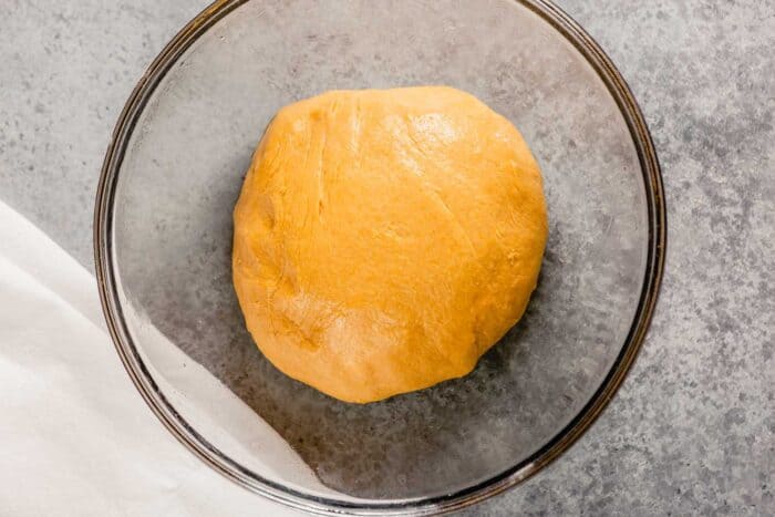 orange colored dough ball in a greased glass bowl