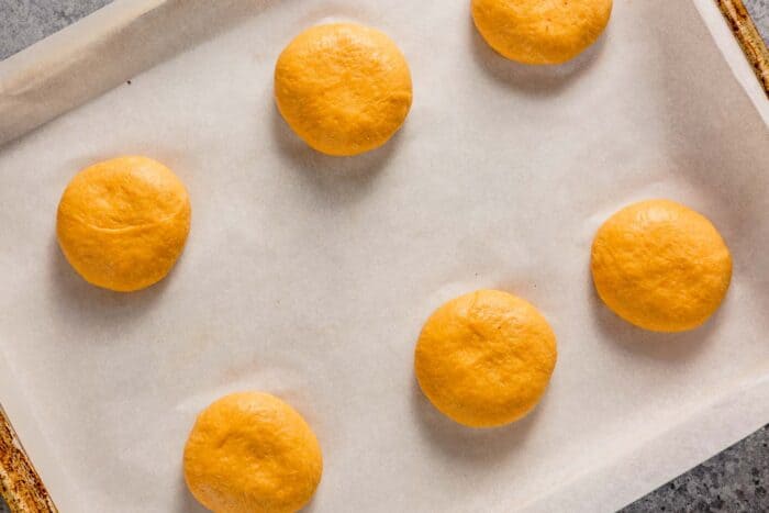 orange colored dough balls on a parchment lined baking sheet