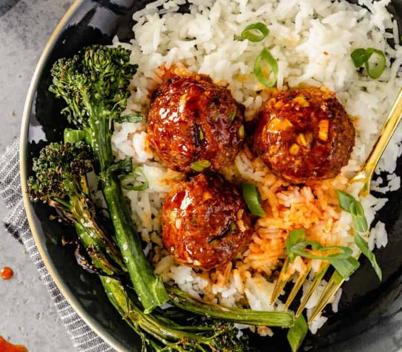 glazed meatballs on a plate of white rice with charred broccolini on the side