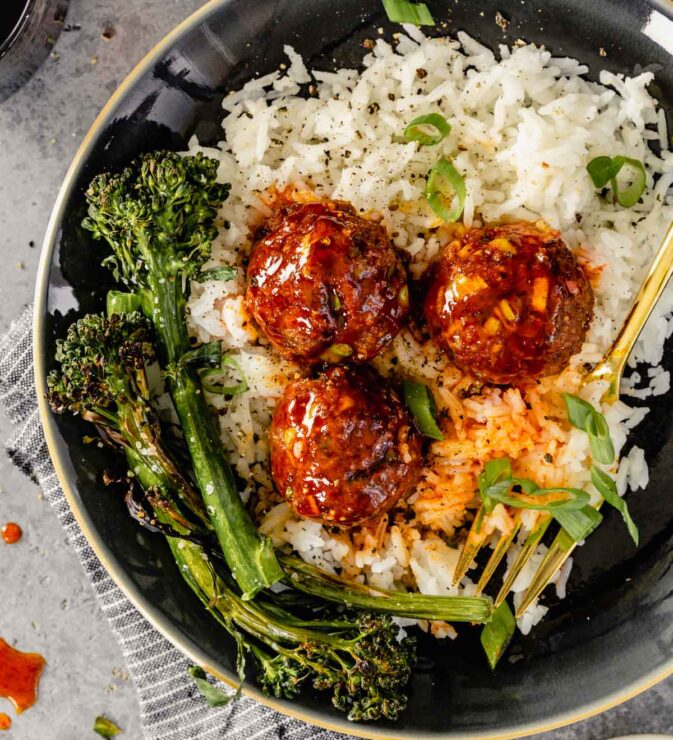 glazed meatballs on a plate of white rice with charred broccolini on the side