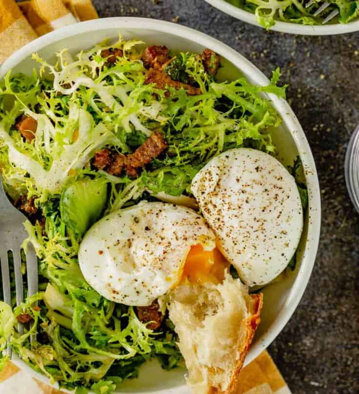 salad in white bowl with bacon lardons and poached eggs