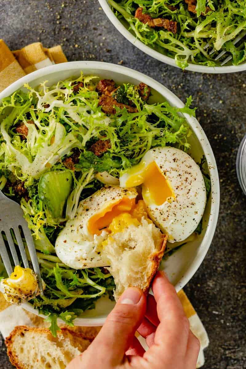 salad in white bowl with bacon lardons and poached eggs