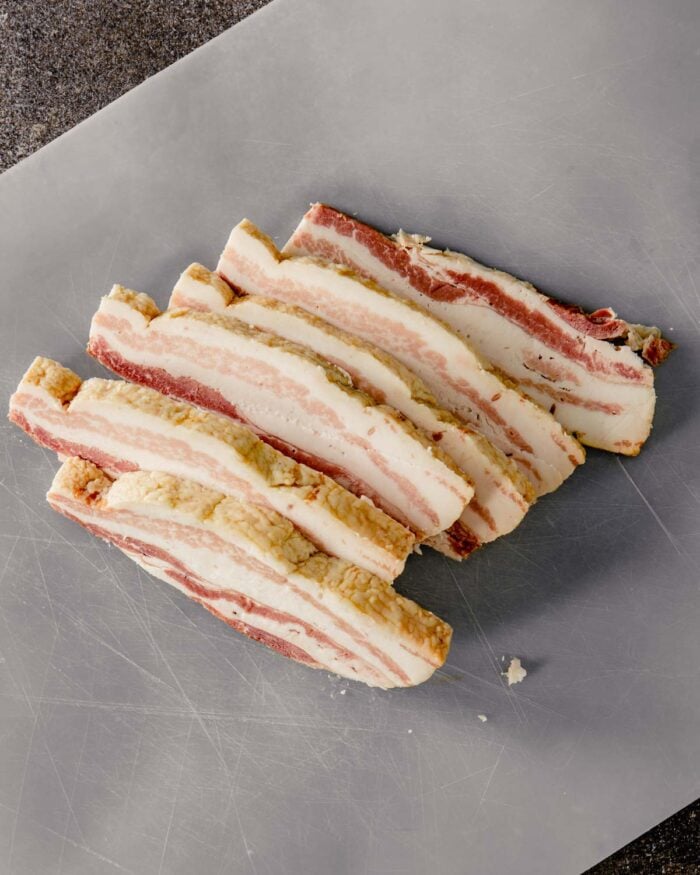 slab bacon sliced into thick strips on a plastic cutting board