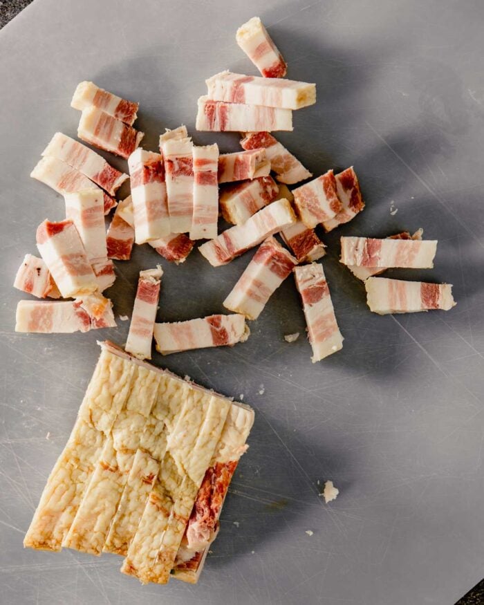 slab bacon cut into lardons on a plastic cutting board