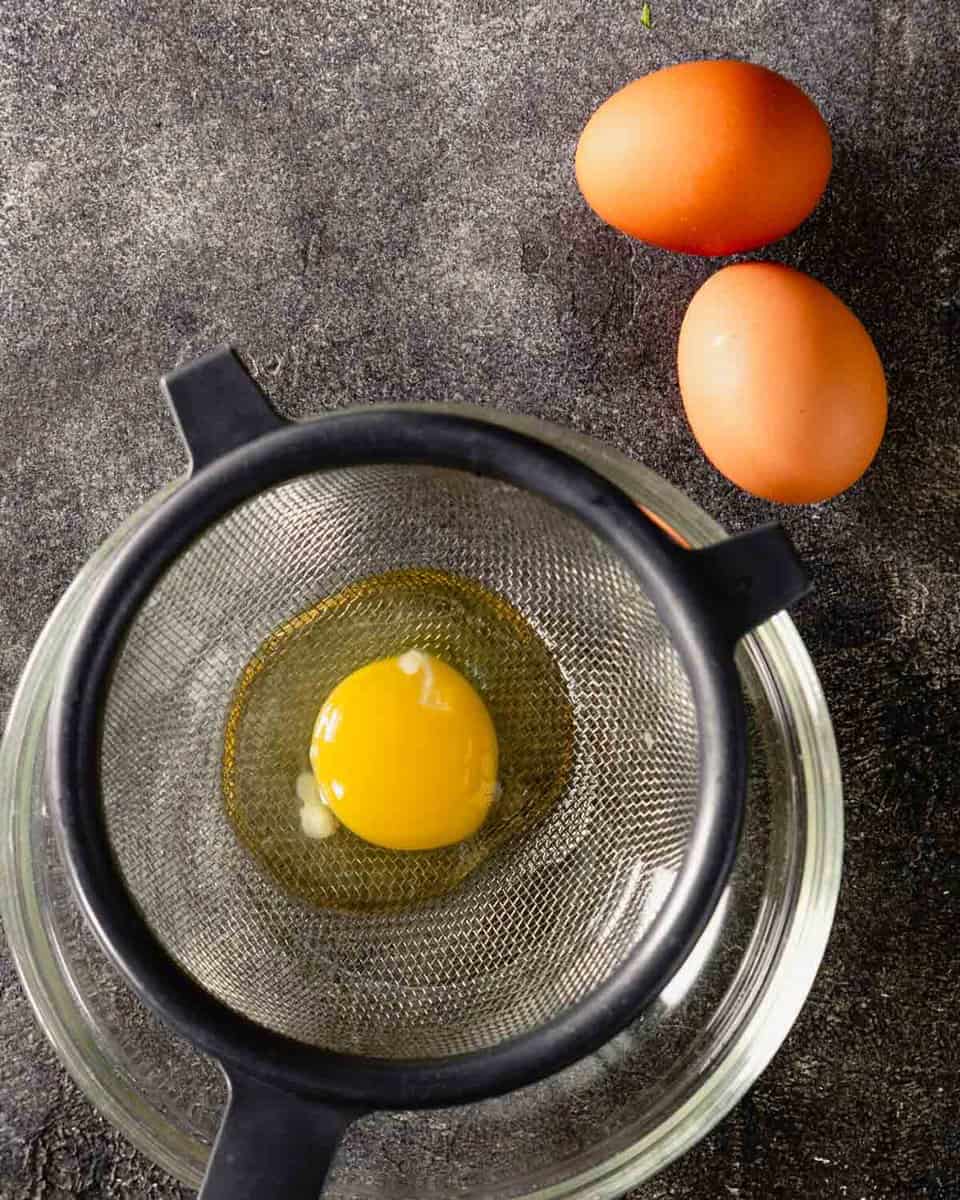 egg draining in a fine mesh sieve set over a glass bowl