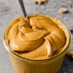 creamy peanut butter in a glass jar with a spoon in it