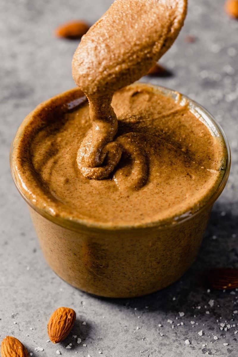 creamy almond butter getting dripped into a clear glass container