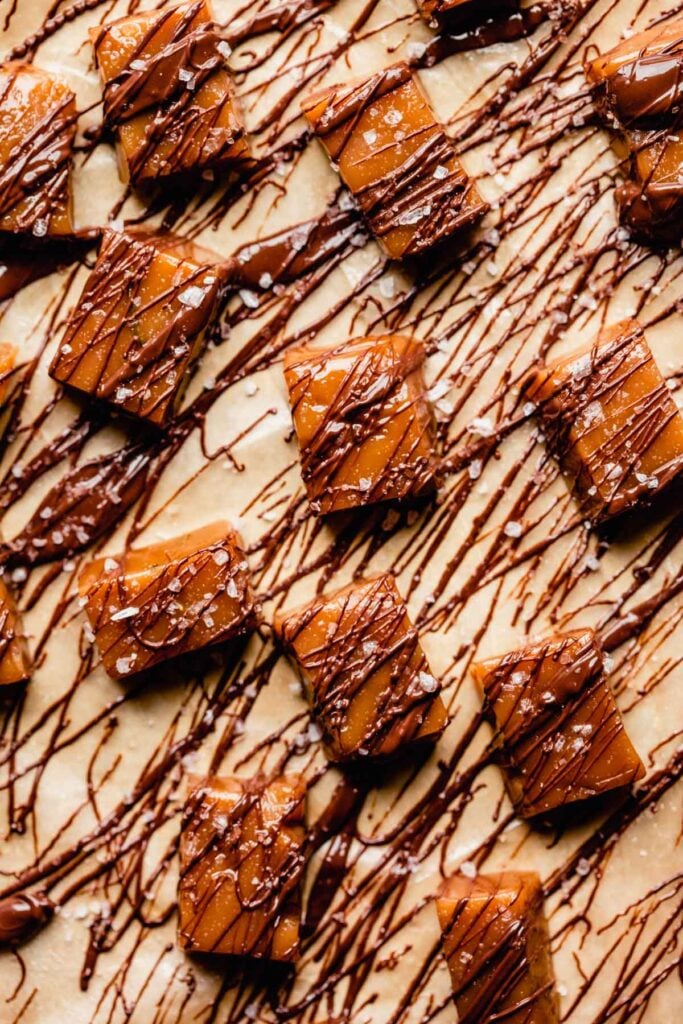 homemade caramels drizzled with chocolate set on brown parchment paper
