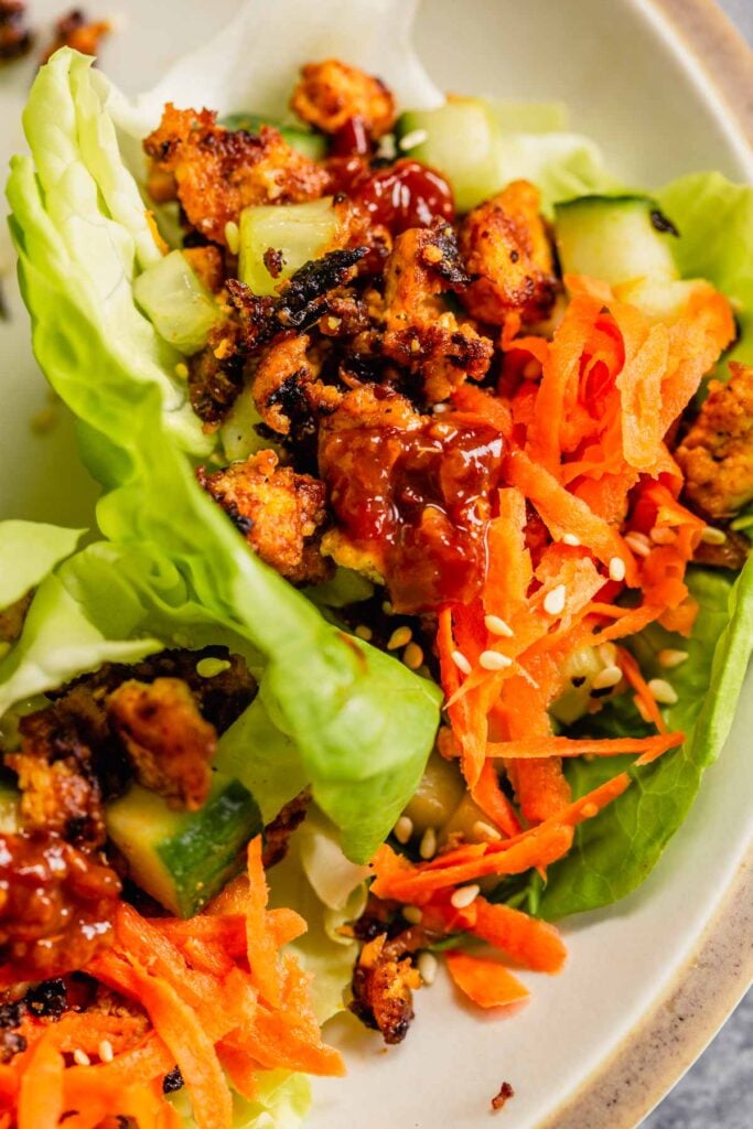 close up of browned tofu in lettuce cups and topped with shredded carrots