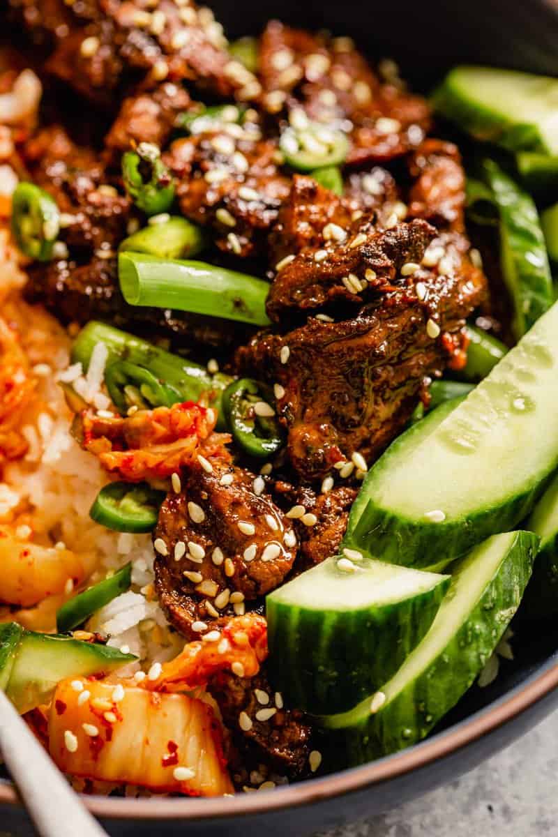 close up image of pork bulgogi in a bowl with rice and sliced cucumber