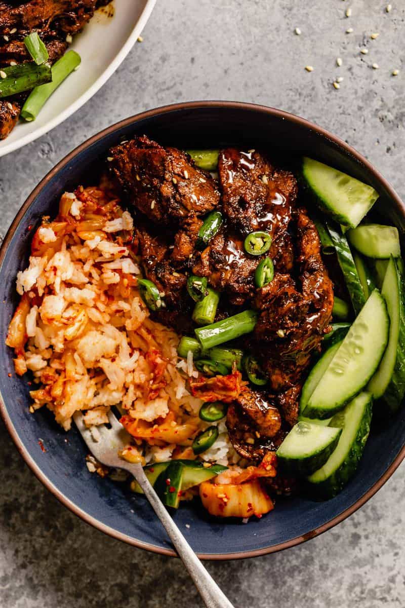 pork bulgogi in a blue dusty bowl with rice and sliced cucumber