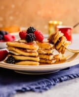 pancakes stacked on a plate with berries on top and maple syrup dripping down