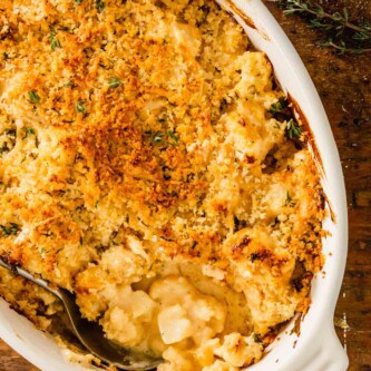 saucy cauliflower in an oval baking dish topped with breadcrumbs