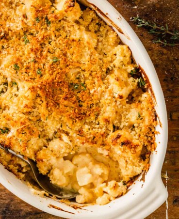 saucy cauliflower in an oval baking dish topped with breadcrumbs