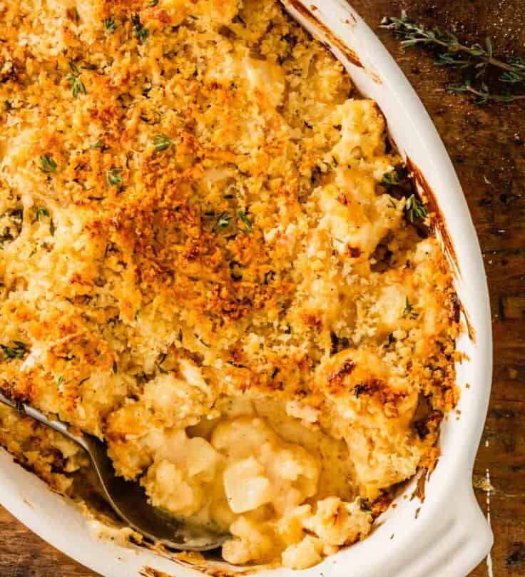 saucy cauliflower in an oval baking dish topped with breadcrumbs