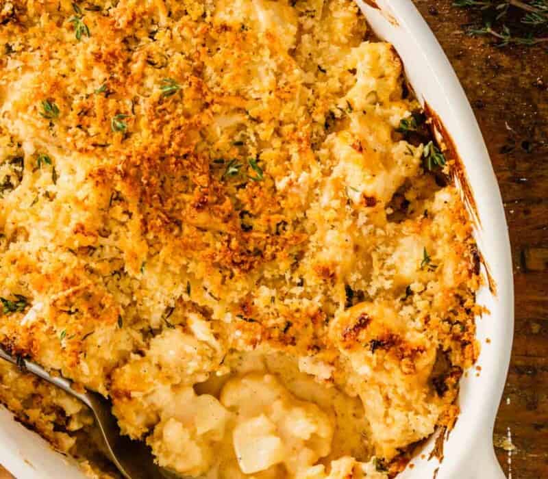 saucy cauliflower in an oval baking dish topped with breadcrumbs