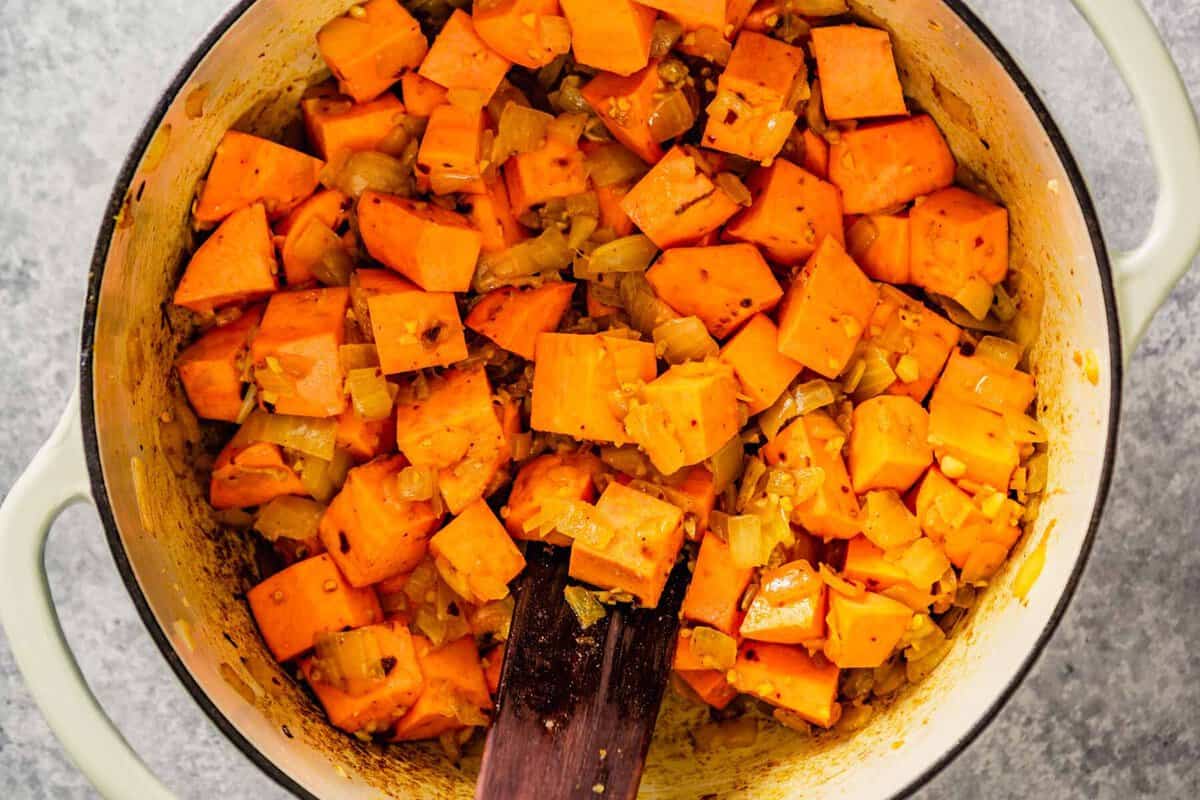 diced sweet potatoes added to a pot with cooked onions and yellow spices