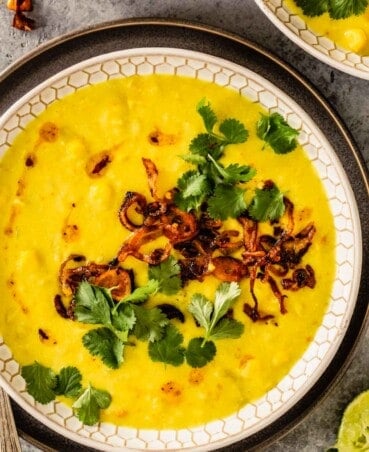 bright yellow soup in a white patterned bowl topped with cilantro and fried shallots