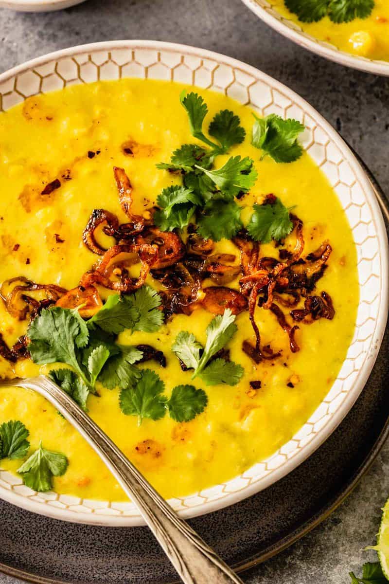bright yellow soup in a white patterned bowl topped with cilantro and fried shallots