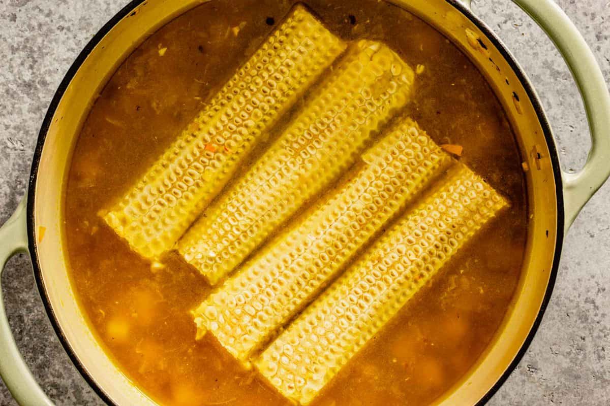 corn cobs with corn kernels removed in a pot of broth