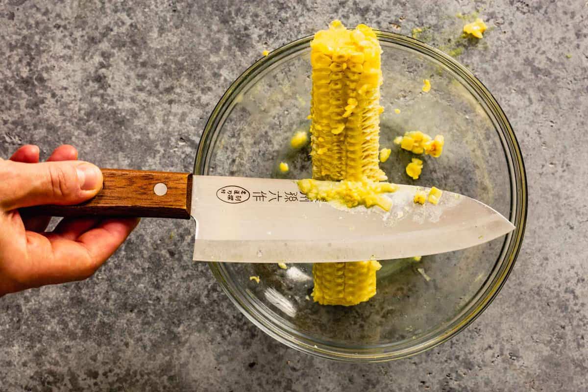 the back of a knife being scraped along a corn cob without corn kernels on it