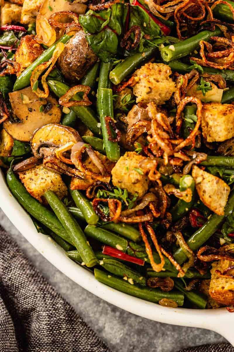 close up of sauteed mushrooms, green beans, croutons and fried shallots in a white dish