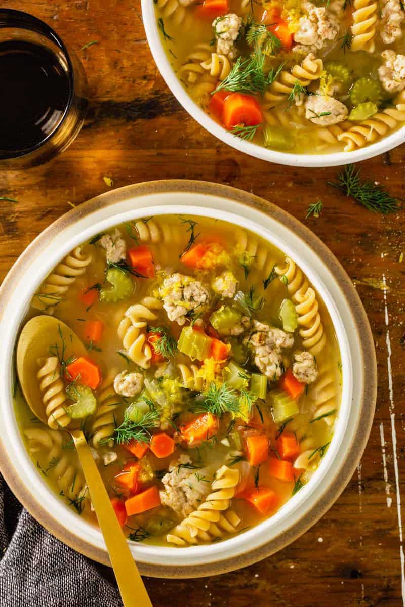 chicken noodle soup in a shallow white bowl set on a wood table