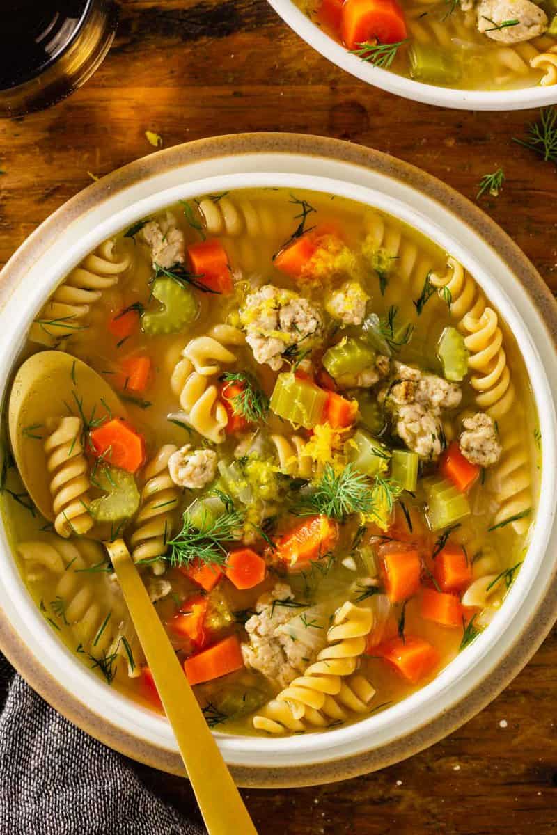 chicken noodle soup in a shallow white bowl set on a wood table